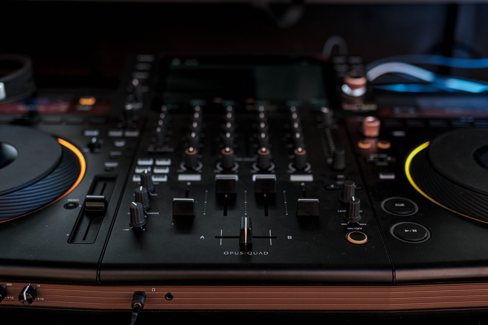 A DJ console under warm light, close on the faders and the jog wheels